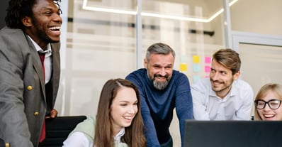 5 colleagues laughing in front of a computer screen