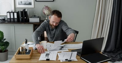 Homme en chandail gris qui travaille avec beaucoup de document devant lui